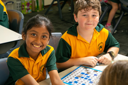 Two students smiling at camera with mathematics booklet in between them.