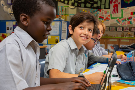 Students typing on devices. One smiling at camera.