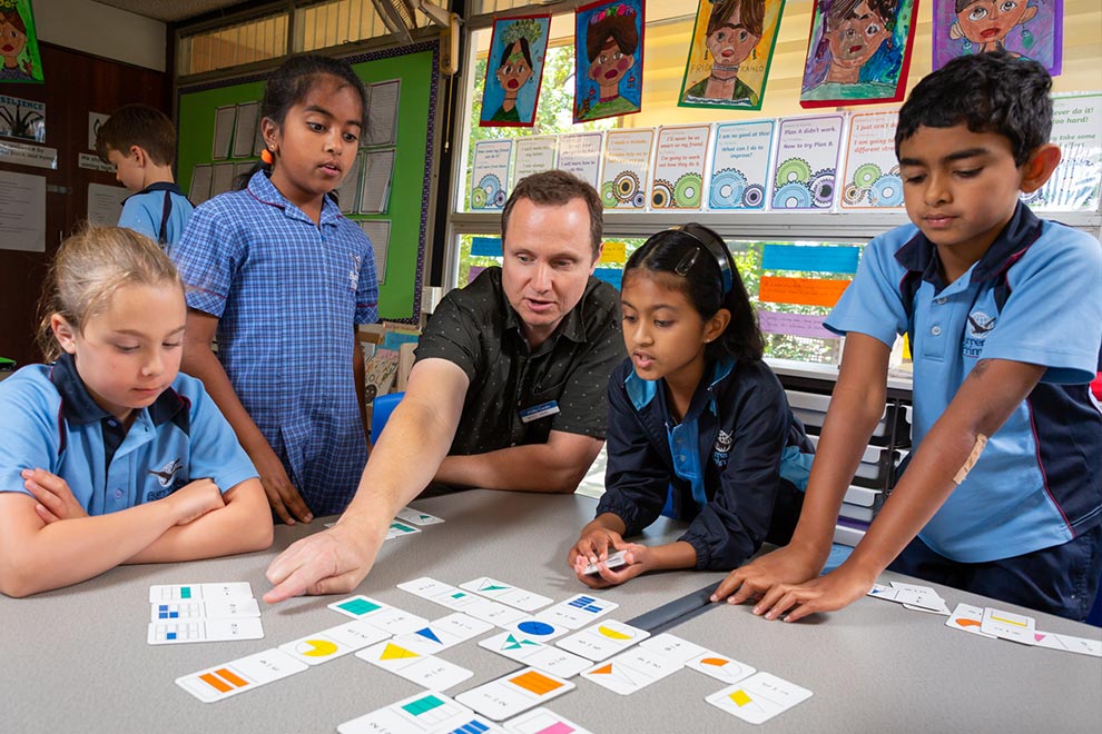 Four students sitting around a table as their teacher points towards a group of cards on the table.