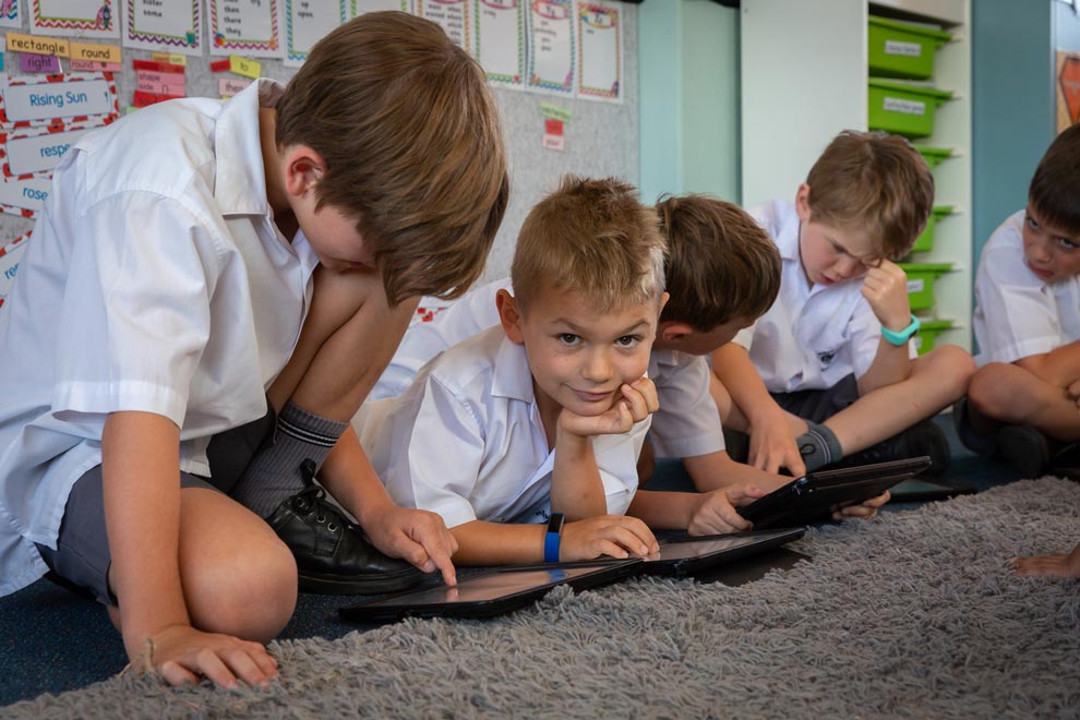 Student looking towards camera while his classmates use tablets